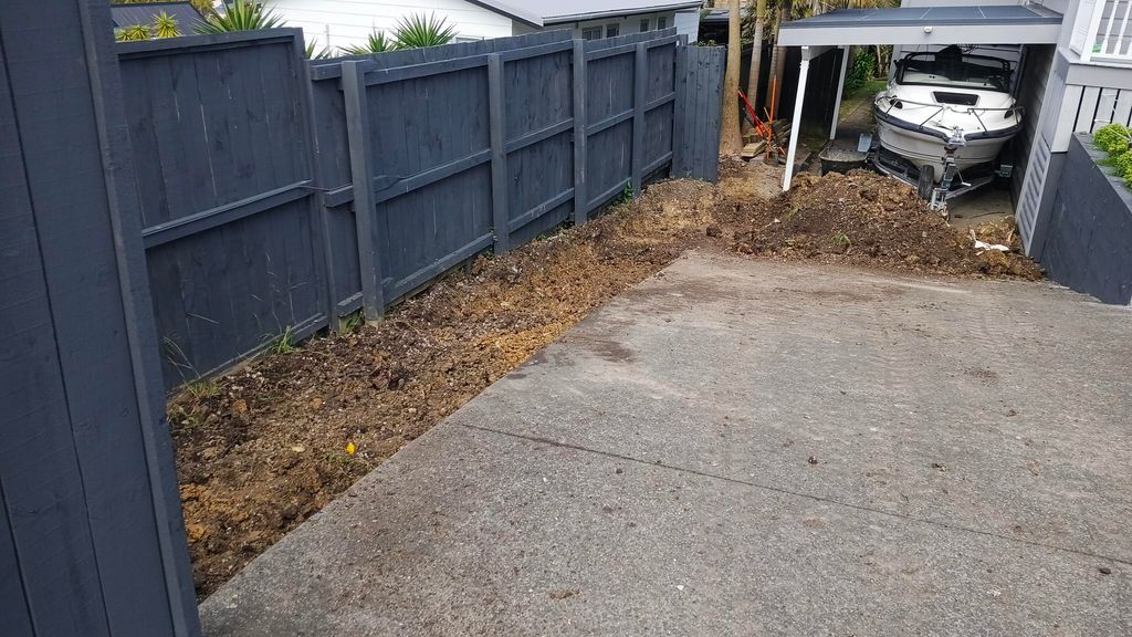 Cleared earth along a driveway edge beside a grey boundary fence