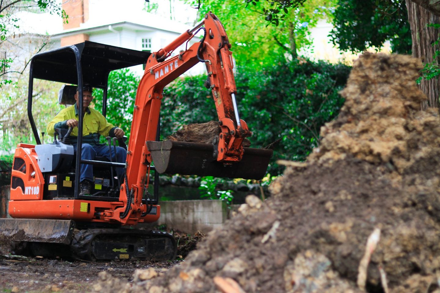 Orange mini digger working beside a pile of excavated earth