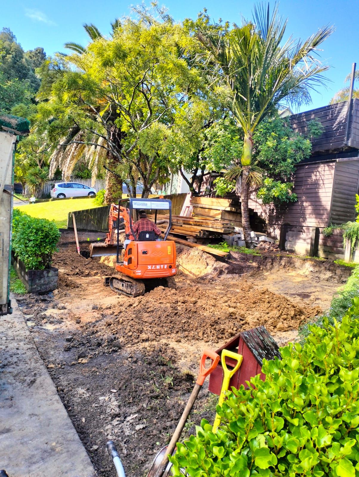 Compact orange digger working in a residential front garden