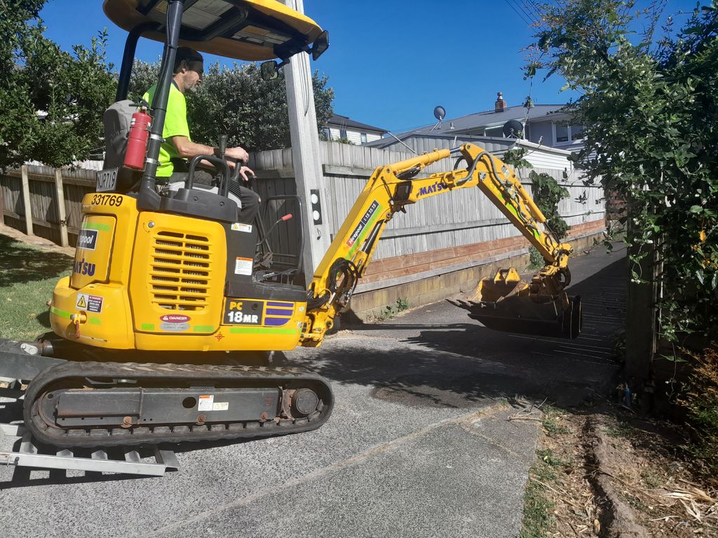 Operator manoeuvring a mini digger through a residential driveway entrance