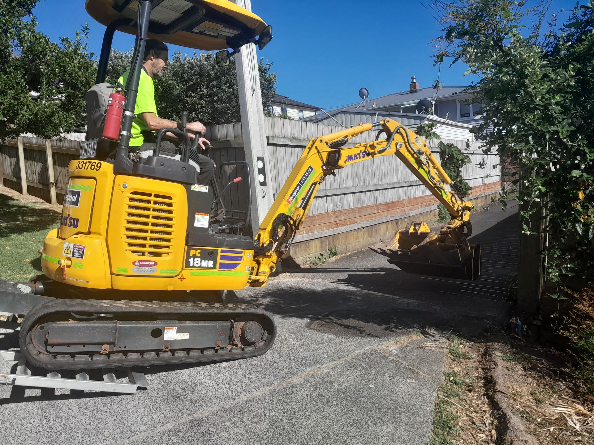 Mini digger and operator working at a residential driveway entrance