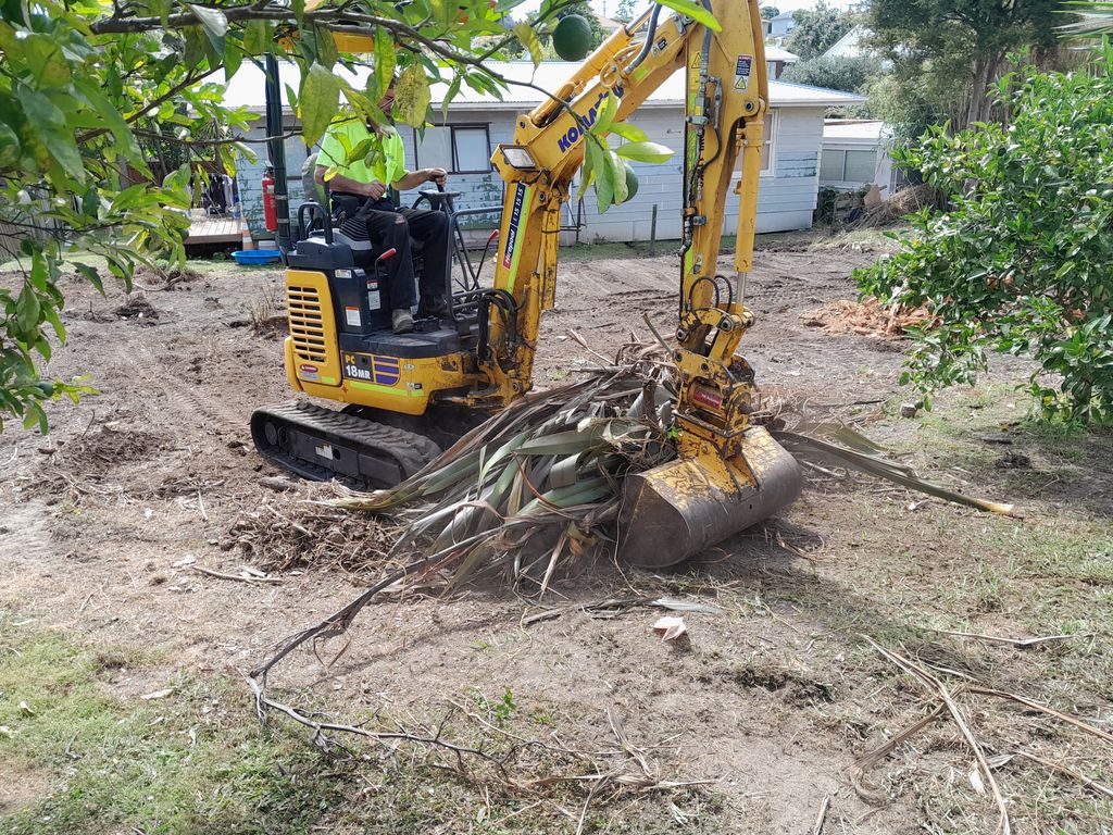 Mini digger lifting uprooted vegetation from a cleared garden