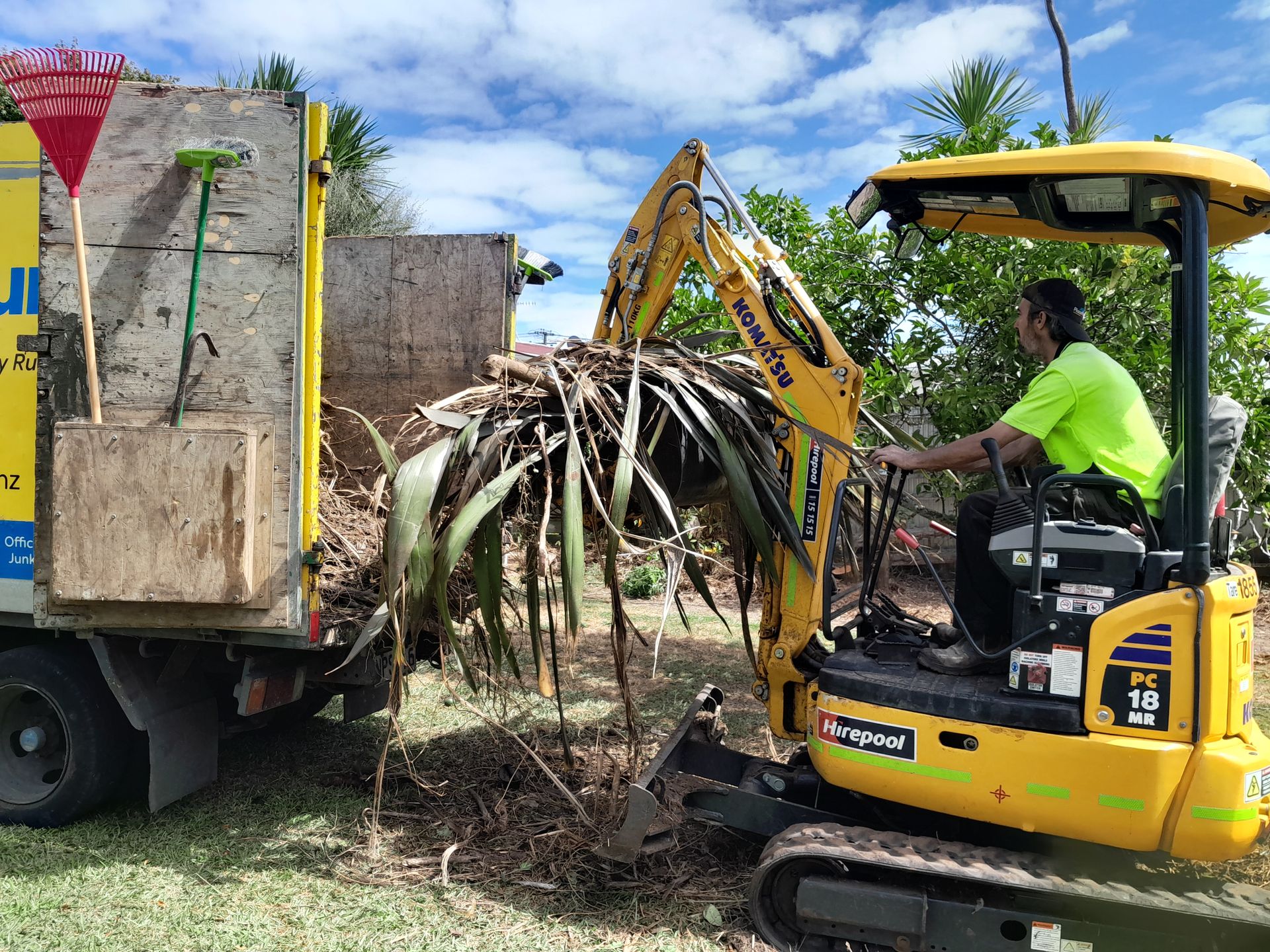 Mini digger loading uprooted garden vegetation into a removal truck