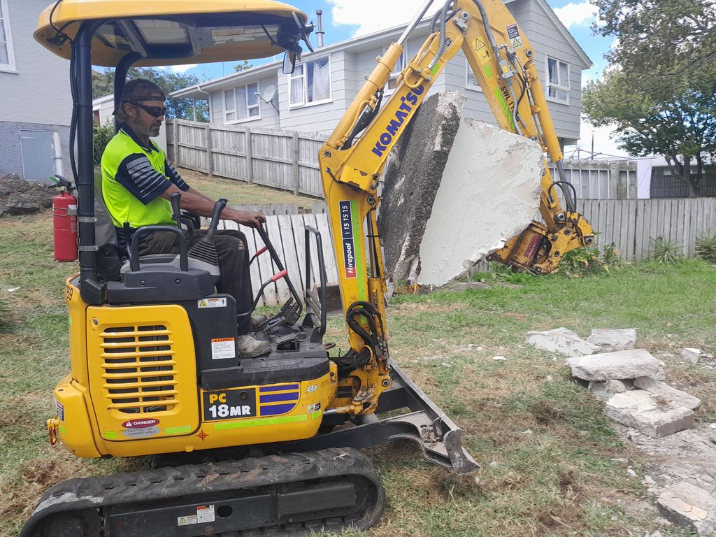 Mini digger lifting a broken concrete slab from a residential property