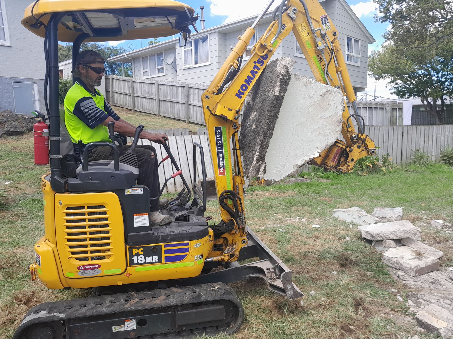 Operator lifting a broken concrete slab with a mini digger