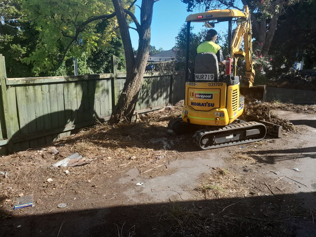 Operator manoeuvring a mini digger alongside a timber boundary fence
