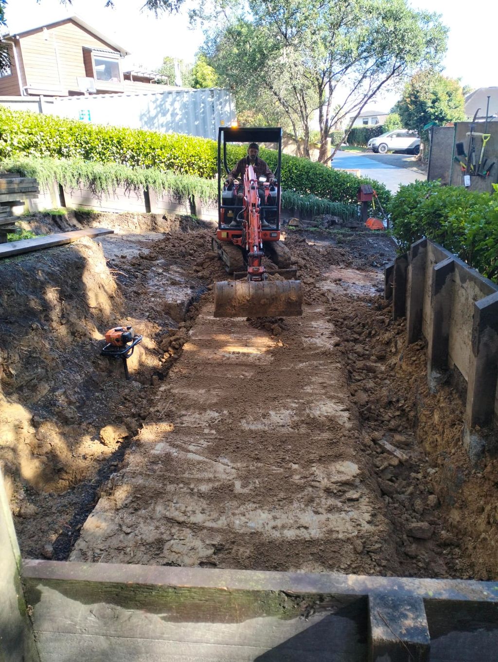Mini digger excavating a narrow area beside a property boundary
