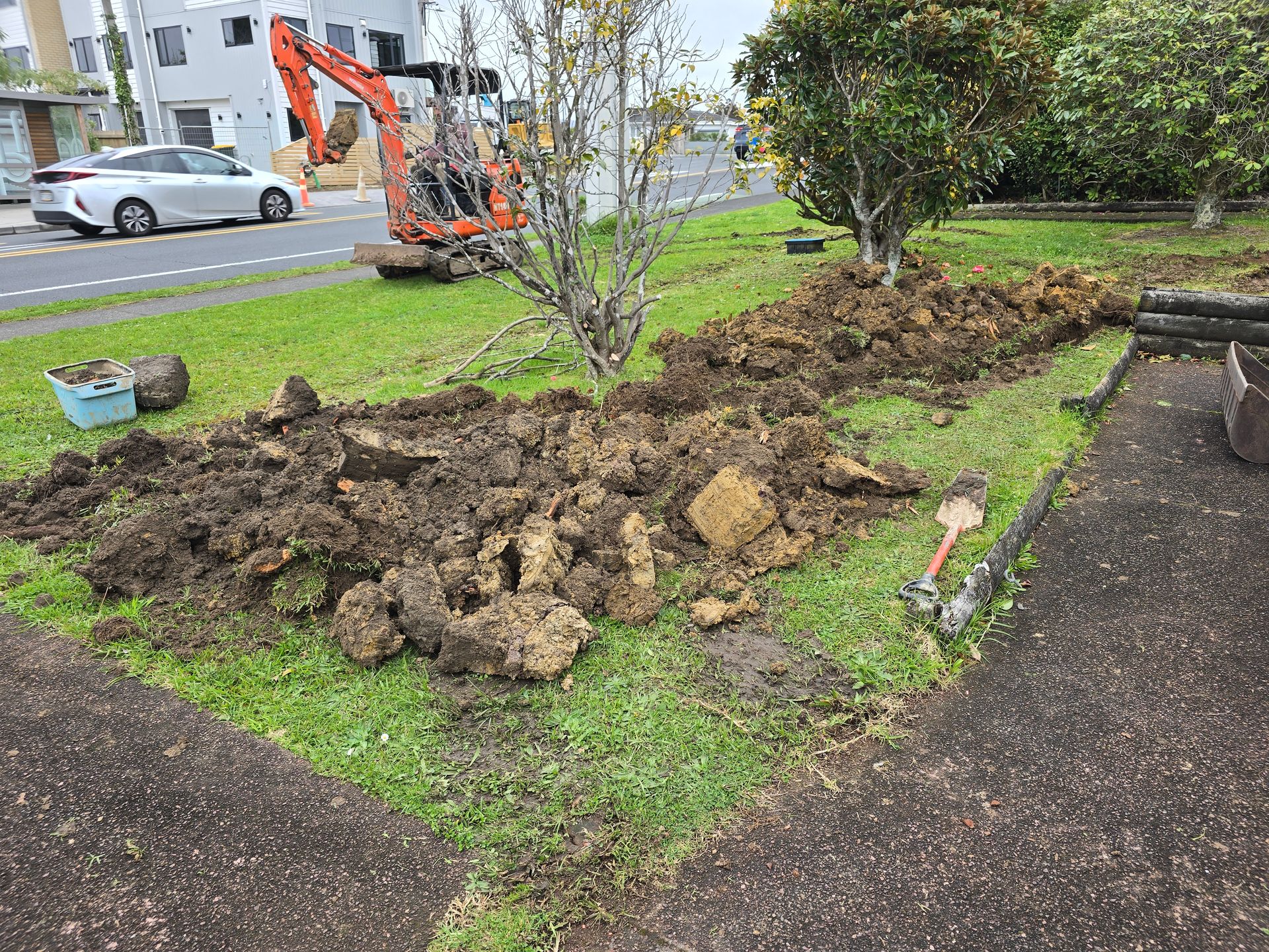 Excavated ground beside a garden path with an orange digger in the background