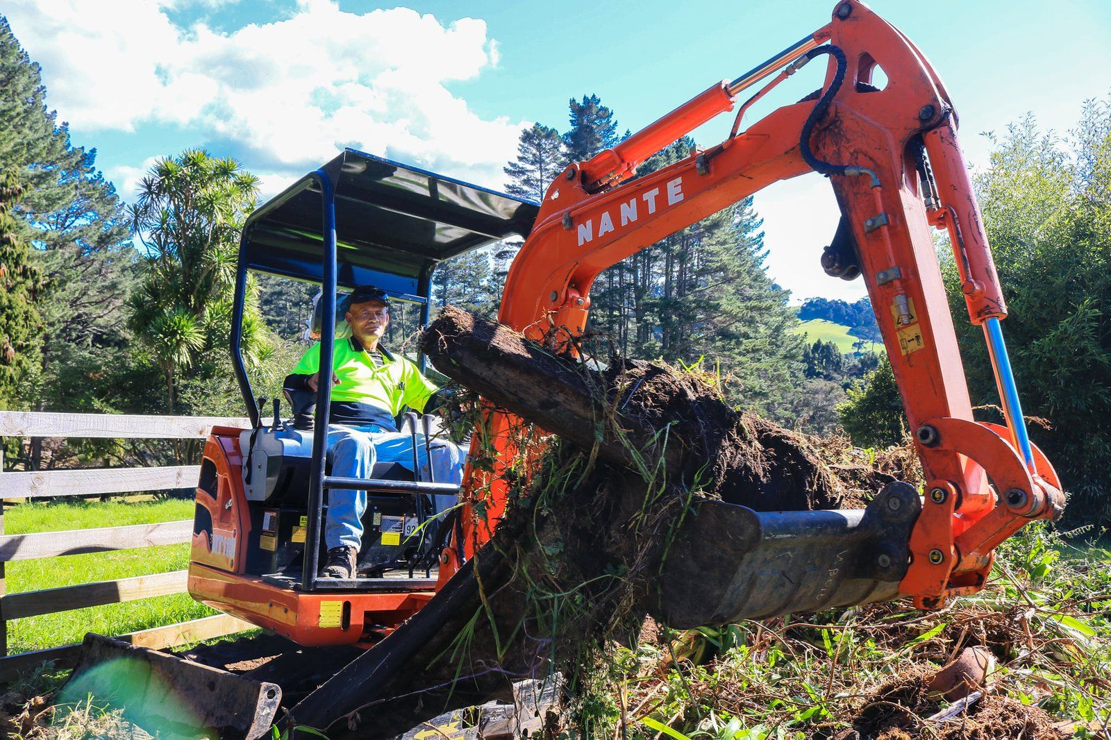 Orange mini digger lifting a tree stump and roots