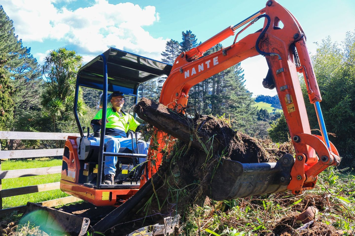 Orange mini digger lifting a tree stump and roots