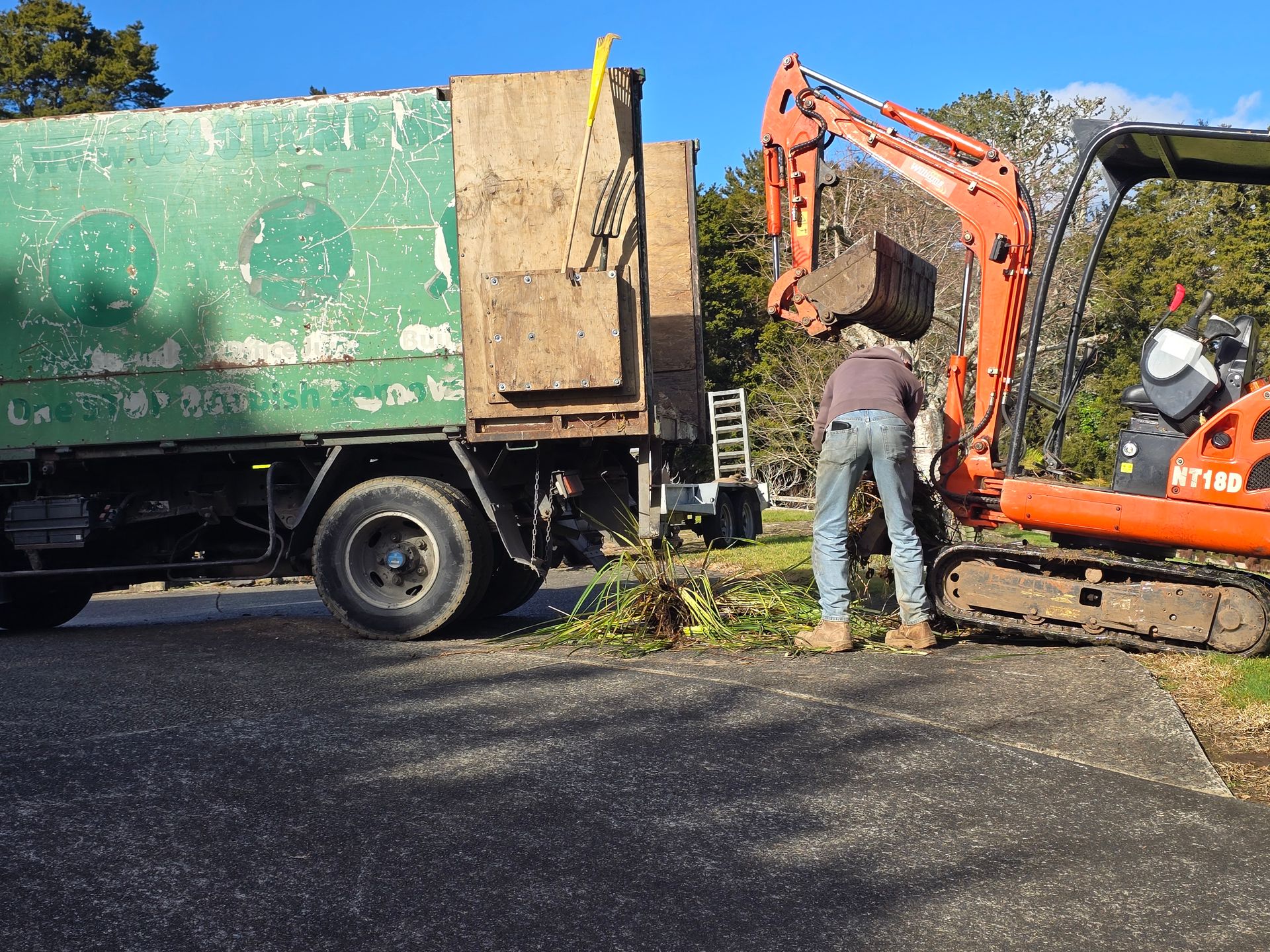 Orange Williams mini digger and crew member beside a removal truck