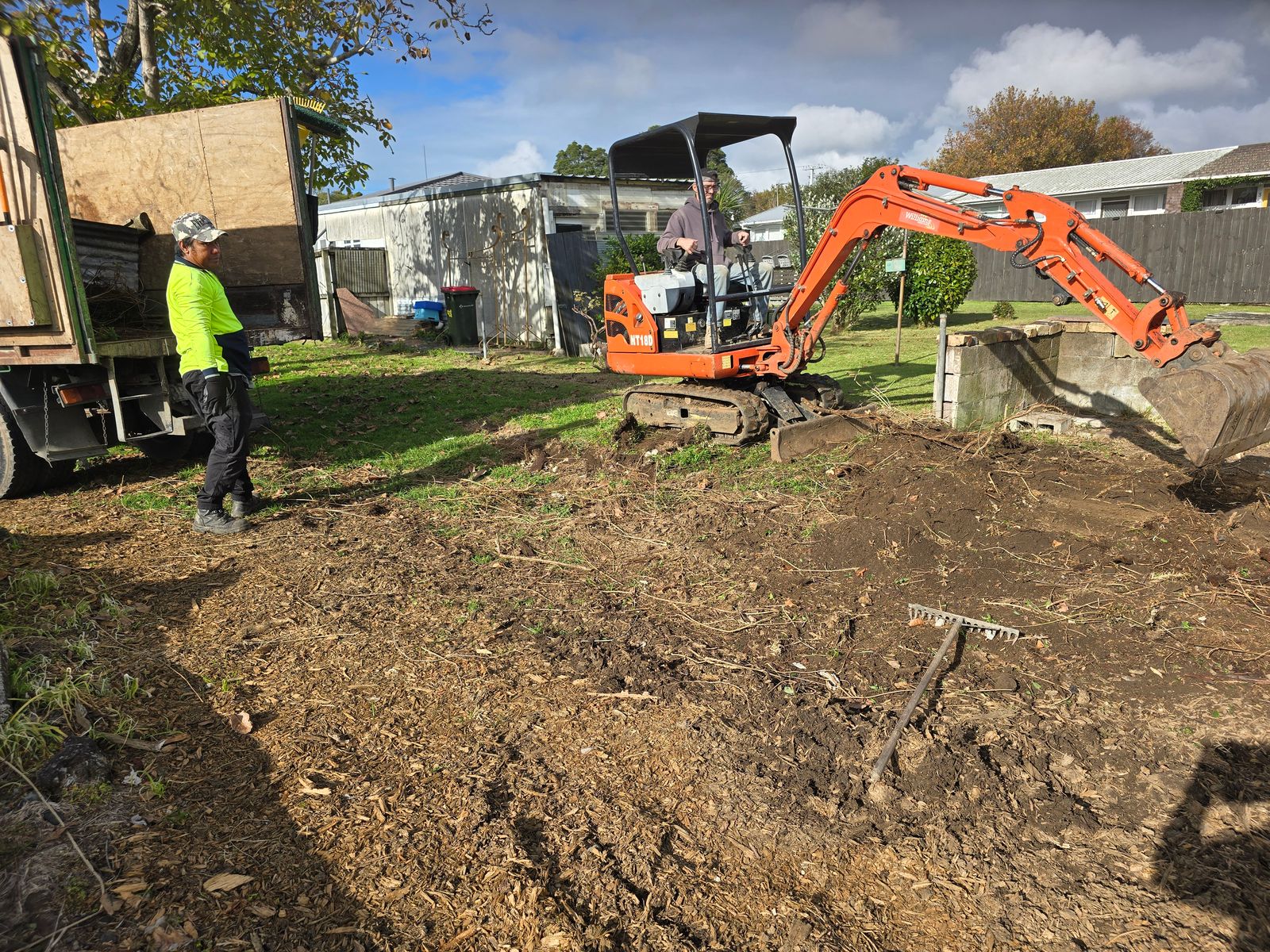 Orange Williams digger working on earthworks beside a crew member and truck