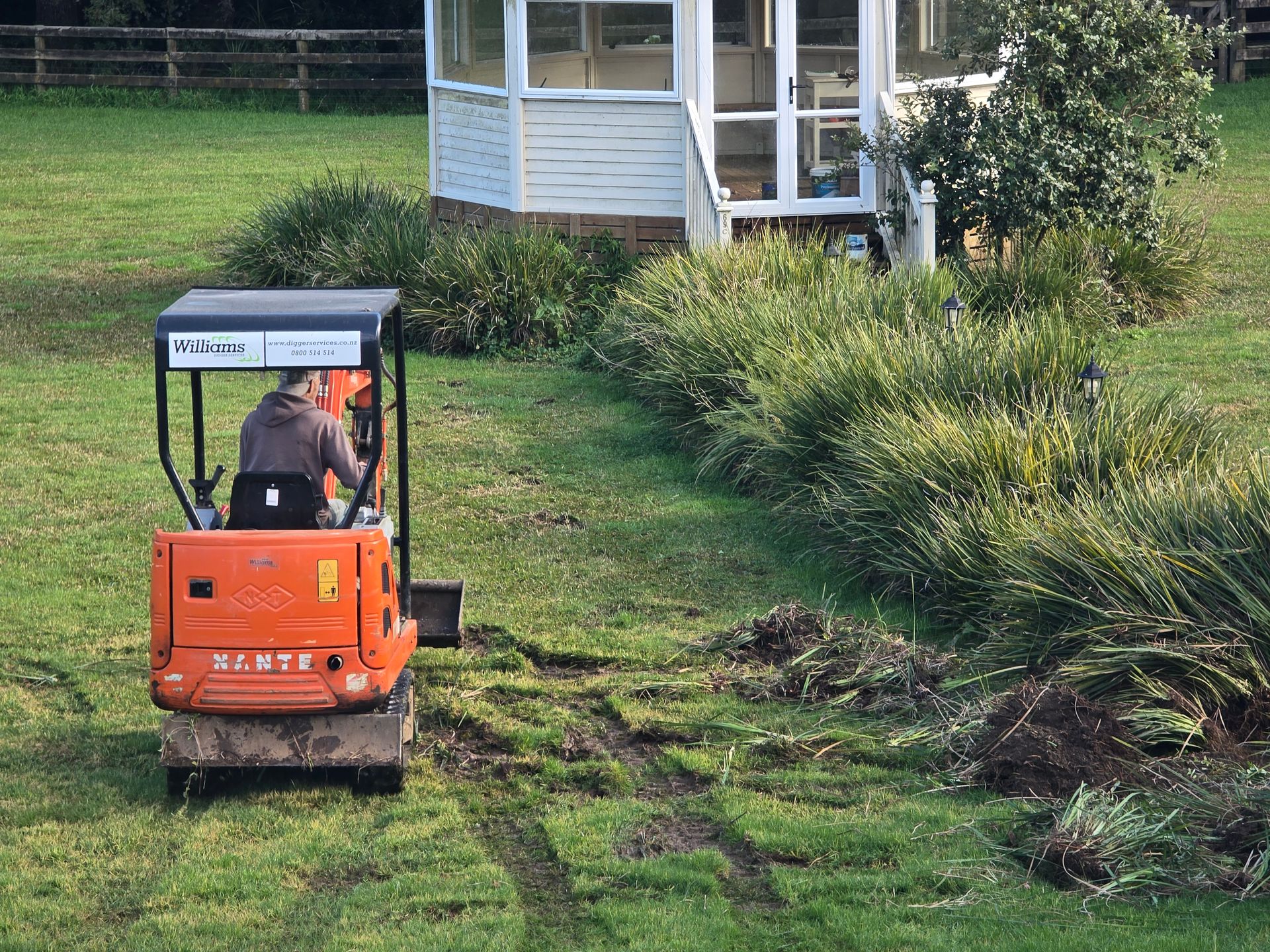 Orange Williams mini digger clearing planting beside a garden gazebo