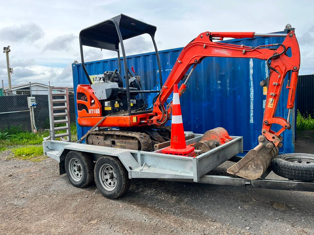 Orange Williams mini digger and attachments on a transport trailer