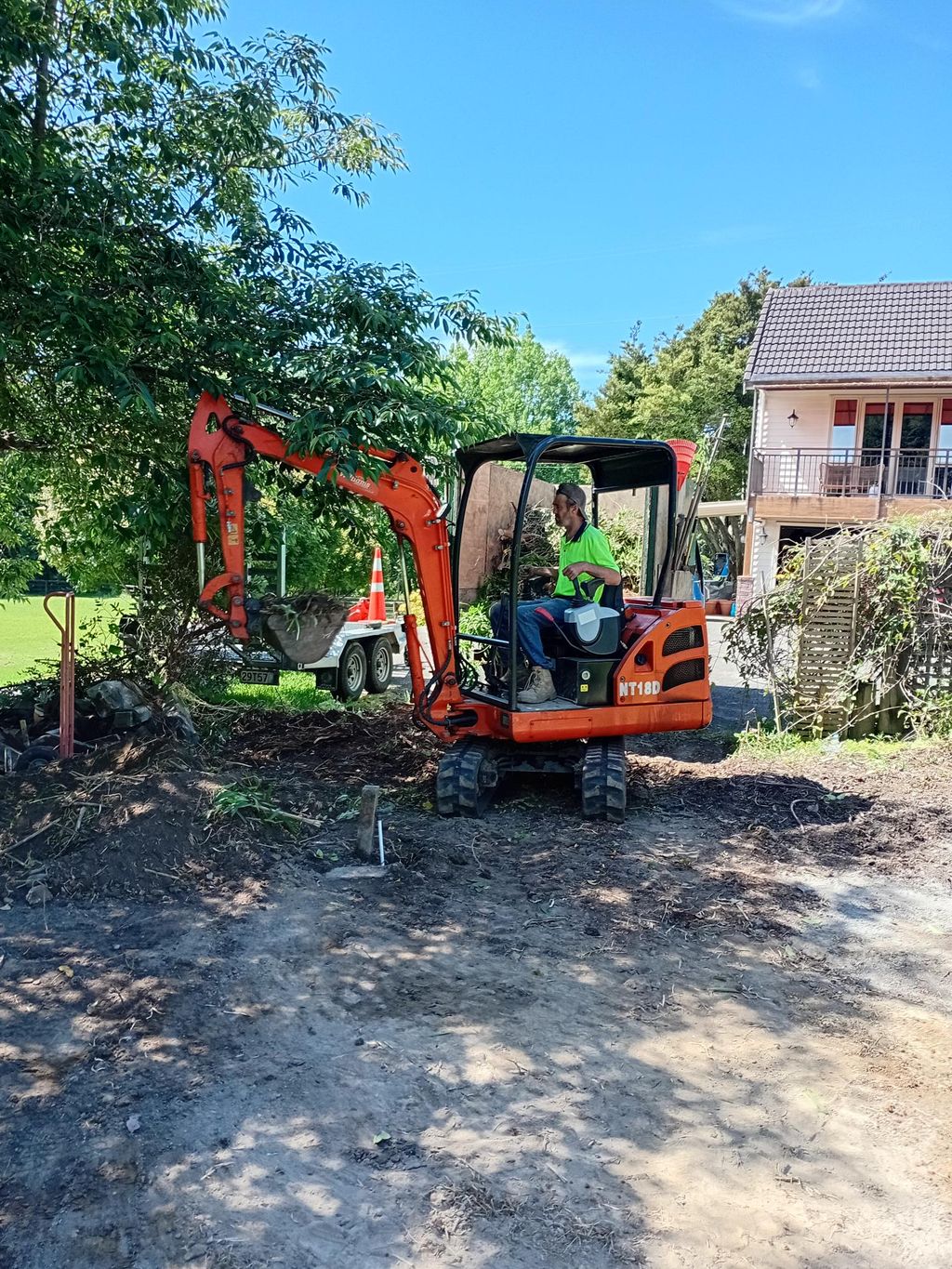 Operator using an orange mini digger to clear ground beside a house